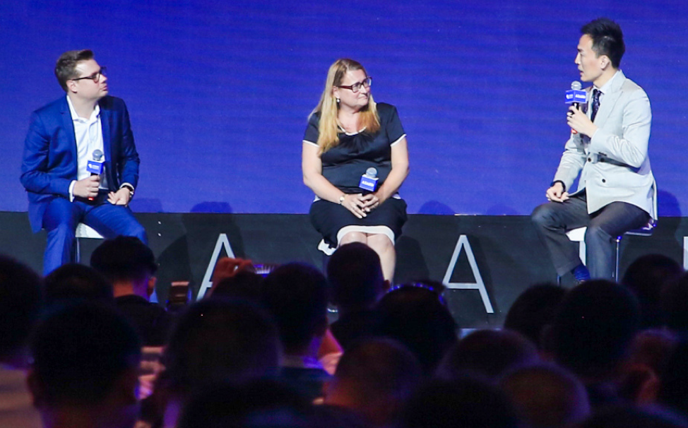 Three people sit on chairs on a stage with microphones